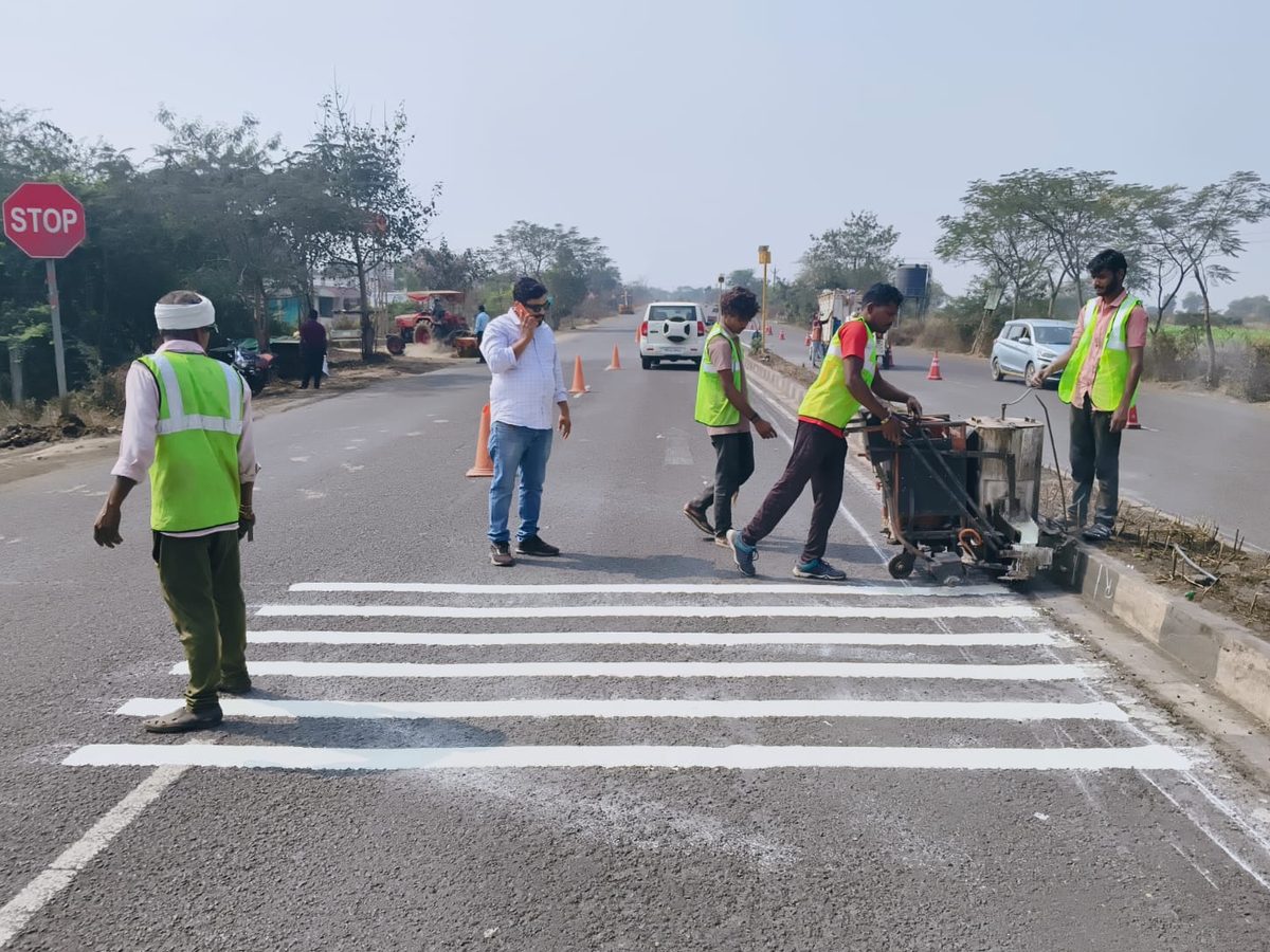 A crew in high-visibility vests applying white bars across a lane with a marking machine