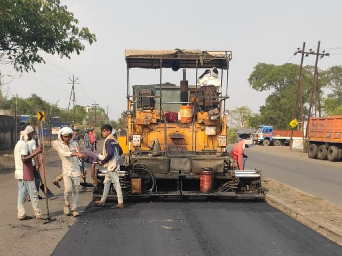 A paver laying fresh asphalt near Padoli, with the crew working beside it